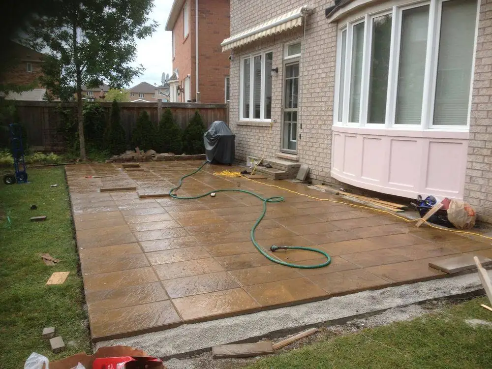 Finished stone patio alongside a house and lawn